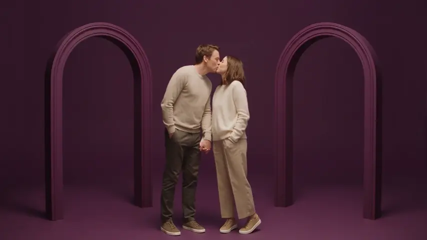 The couple holds hands and shares a kiss in front of the arches